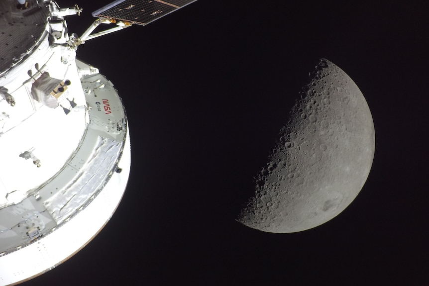 The outside of a spacecraft and the Moon, half in shadow.