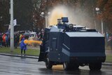 An armoured police vehicle fires a water cannon at people as they flee.