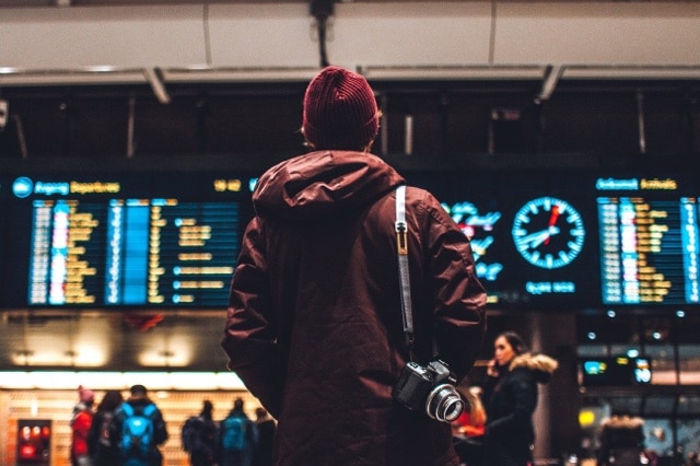 A man in a beanie looks at an airport departure board for a story about lending money to friends.