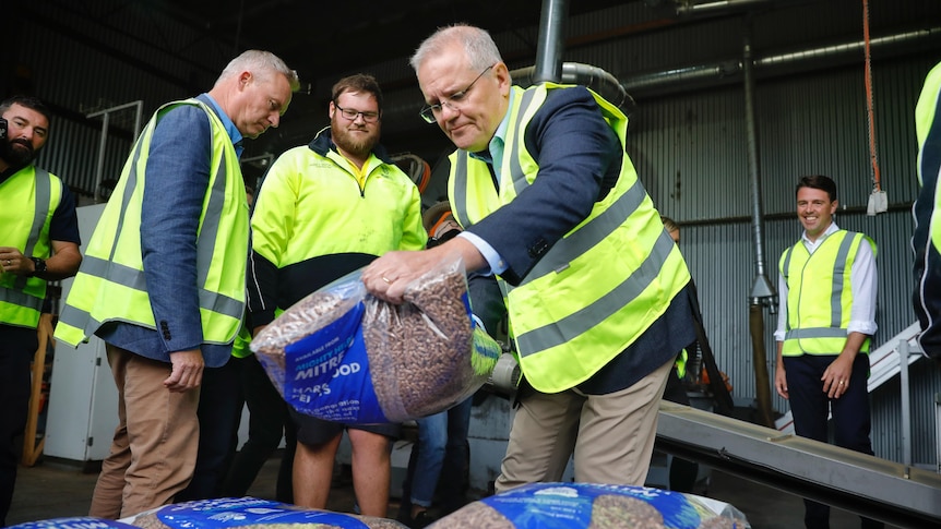 Scott Morrison carries a sack of pellets while wearing yellow high-vis.