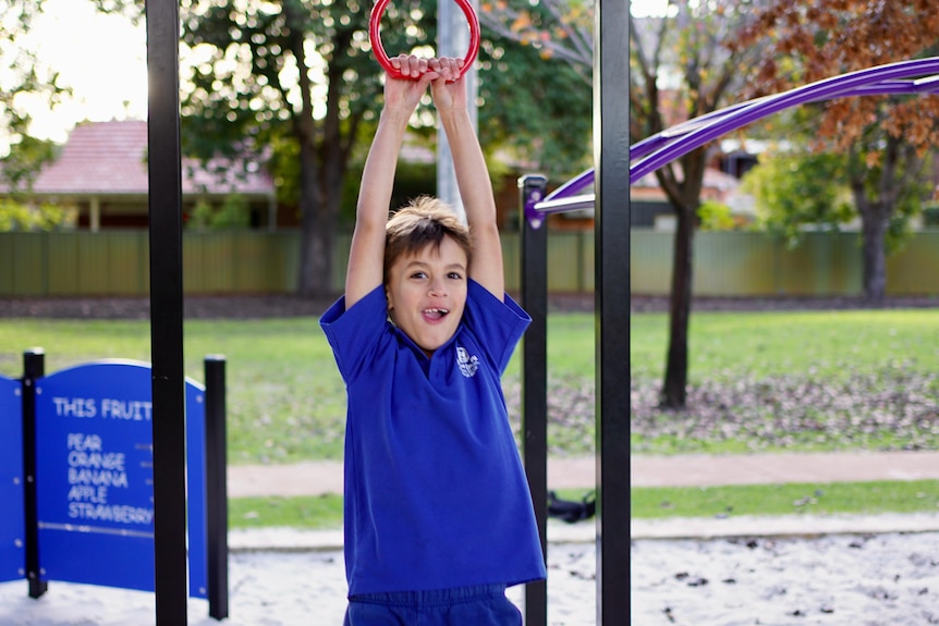 A young white boy swinging from a playground with a smile on his face
