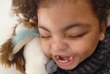 Close-up photo of profoundly disabled child, Chanté, holding a stuffed rabbit.