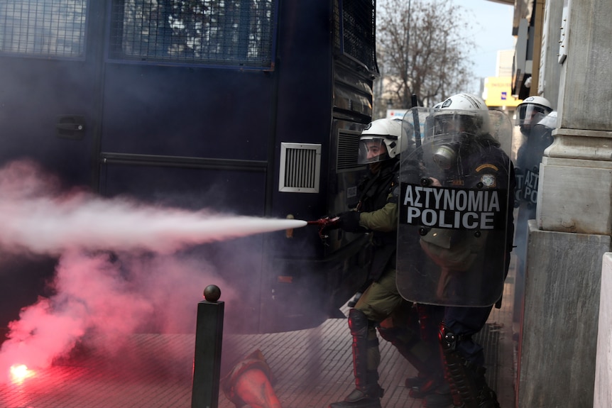 Riot policemen holding shields spray tear gas.