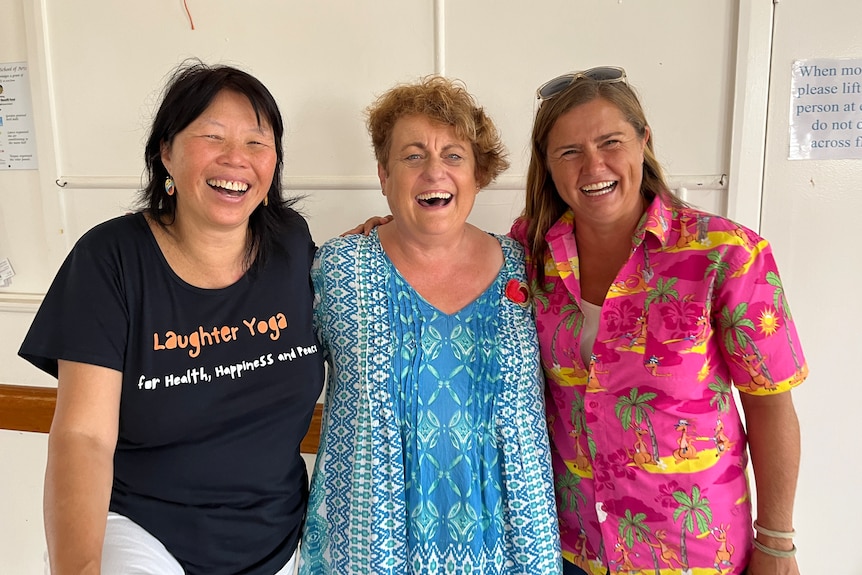 Three women stand together, arms around one another, they are all laughing.