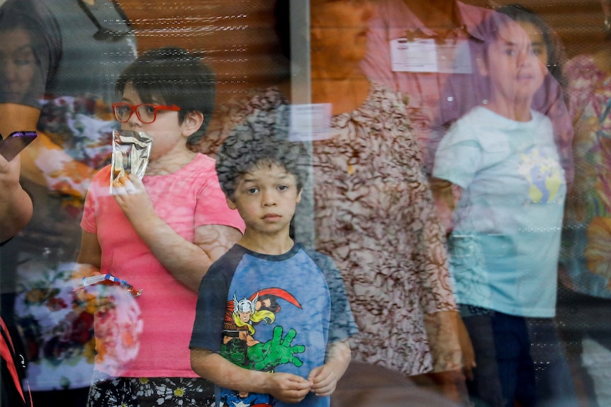 A child looks through a glass window surrounded by other children.