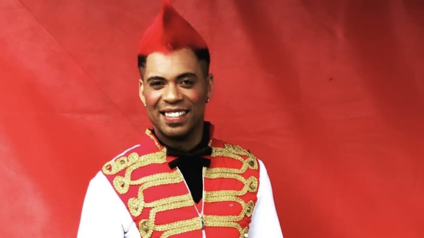 A man in a red vest and hat stands smiling at the camera