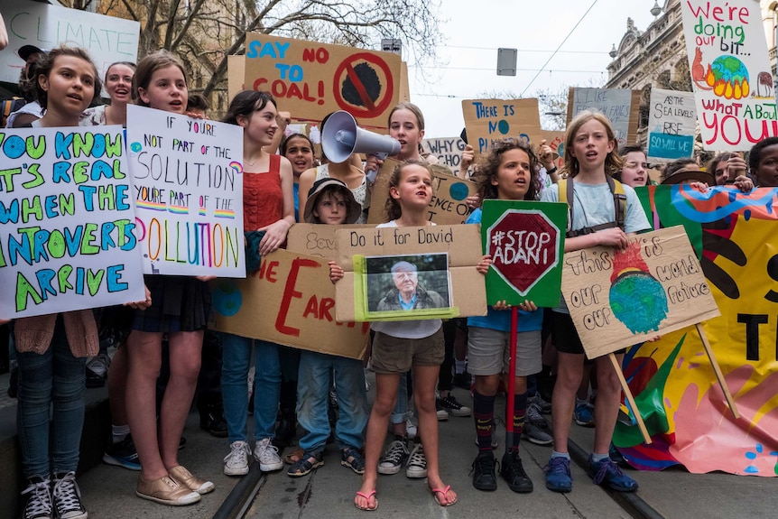 Children stand across tram tracks in Melbourne holding signs with climate change slogans.