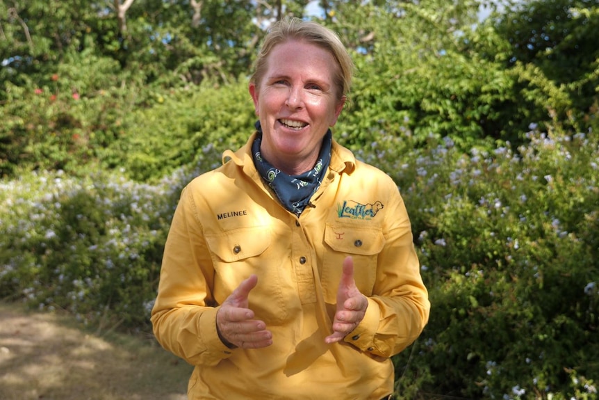 A woman smiles talking, she's wearing a bright workshirt with her name and Leather Cattle Co embroidered with a neck scarf