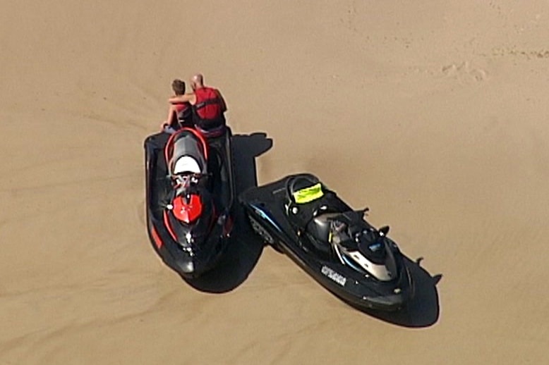 A man puts his arm around a boy on a South Stradbroke Island beach shortly after a person died reportedly falling off a jetski.