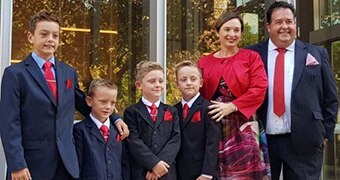 Four young boys, and a woman and man stand close together dressed formally and smiling widely.