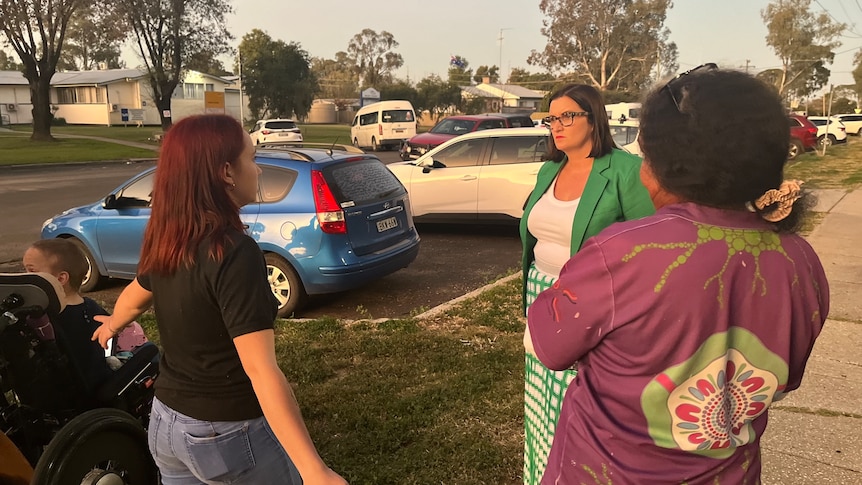 Three women stand in a circle talking on a sidewalk