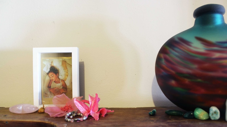 Chanté's photo in a frame, surrounded by pink flowers, next to an urn on top of a cupboard.