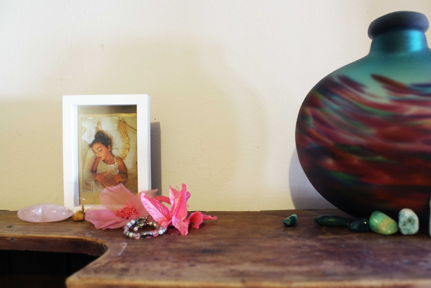 Chanté's photo in a frame, surrounded by pink flowers, next to an urn on top of a cupboard.