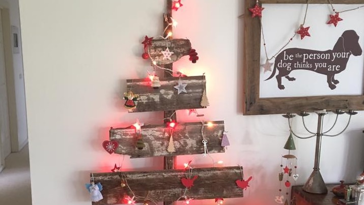 Lights and decorations are hung on old pieces of wood that have been nailed together to form the outline of a Christmas tree.