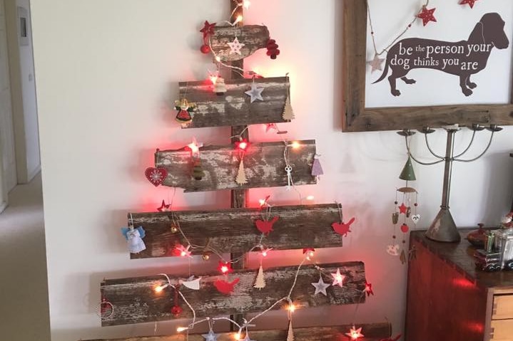 Lights and decorations are hung on old pieces of wood that have been nailed together to form the outline of a Christmas tree.