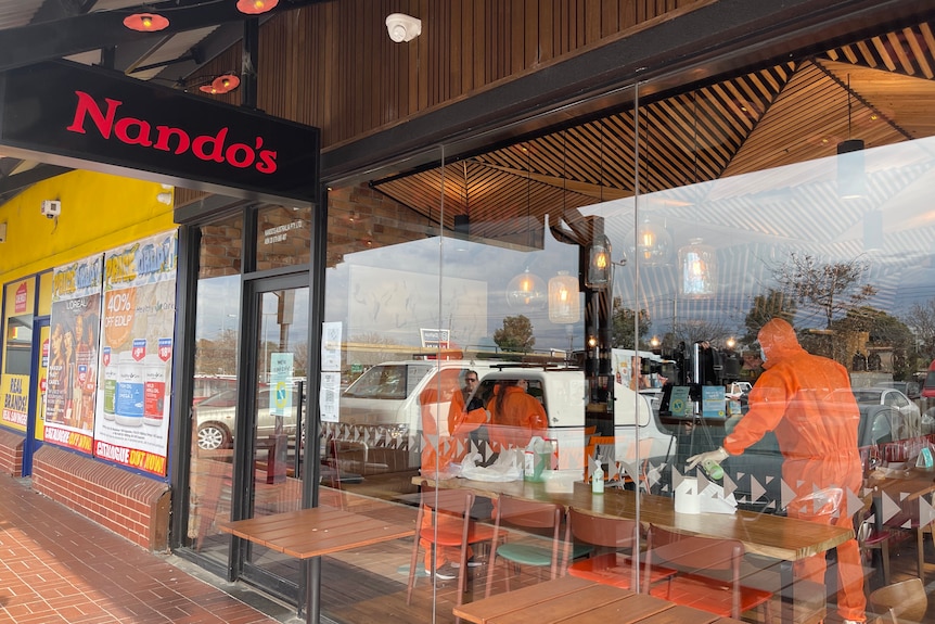 People in full orange PPE clean a Nando's restaurant.