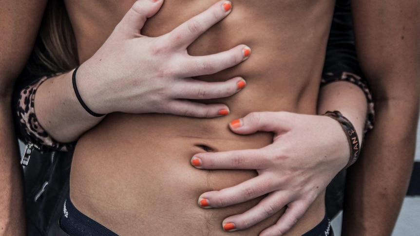 Close-up of man's torso with woman's arms wrapped romantically around him.