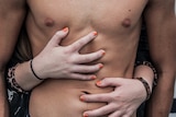 Close-up of man's torso with woman's arms wrapped romantically around him.