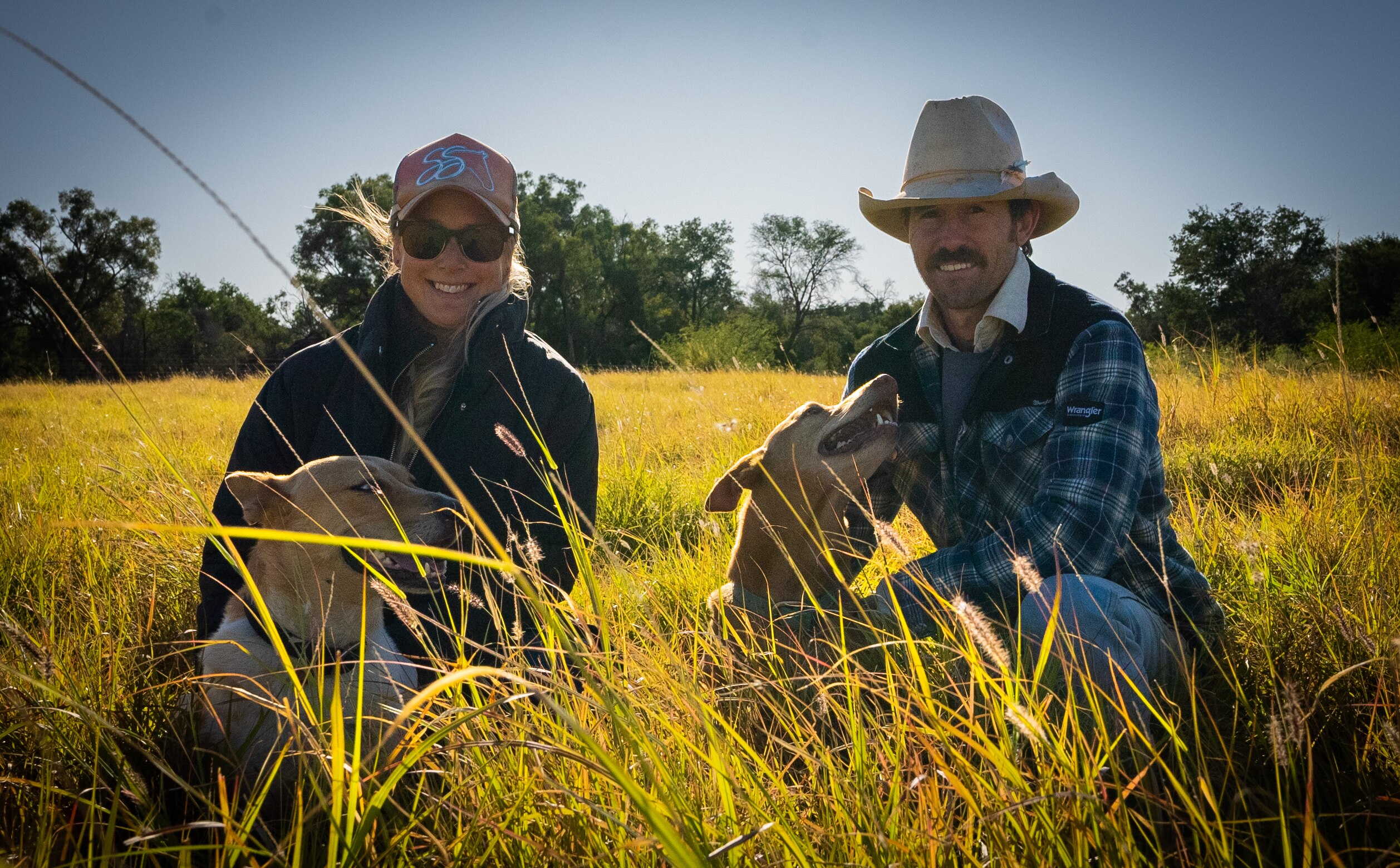 Sam and Alina Hart crouched down in long green and yellow grass at Muttama south of Barcaldine.