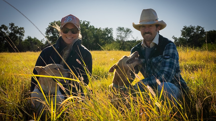 Sam and Alina Hart crouched down in long green and yellow grass at Muttama south of Barcaldine.
