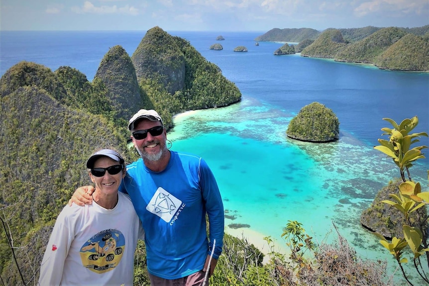 Couple wearing sunglasses on top of a tree-covered volcanic mountain with scenic turquoise bay below