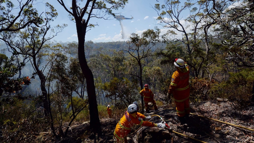 Firefighters look on as a helicopter drops water to contain a spot fire near Faulconbridge on October 23, 2013