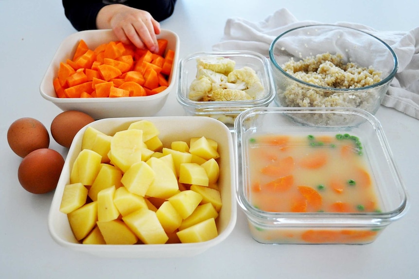 Containers of chopped vegetables, soup and cooked quinoa accompanied by boiled eggs.