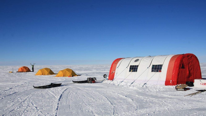 One large red and white, and three small yellow tents on a field of snow in Antarctica