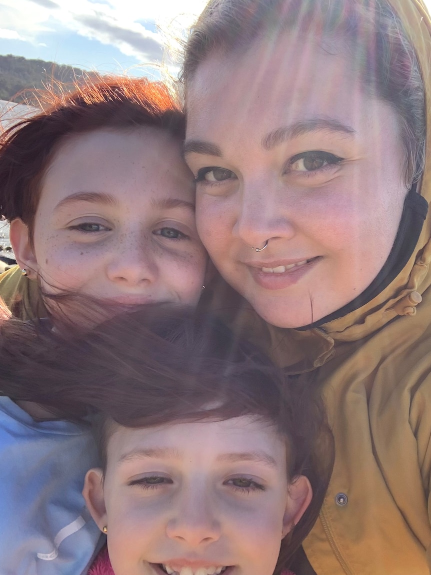 Woman and two kids huddle together and smile at the camera 