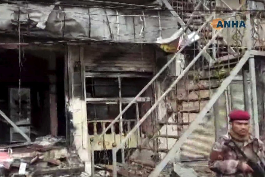 A shop front lays in pieces with debris strewn all over the area and blood smears on the walls.