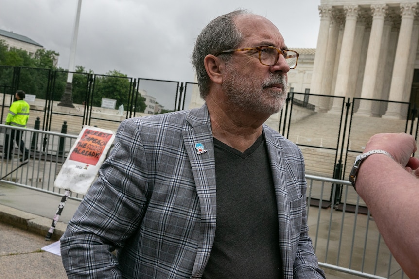 A man wearing glasses, a checked jacket and a T-shirt, stands outside the US Supreme Court.