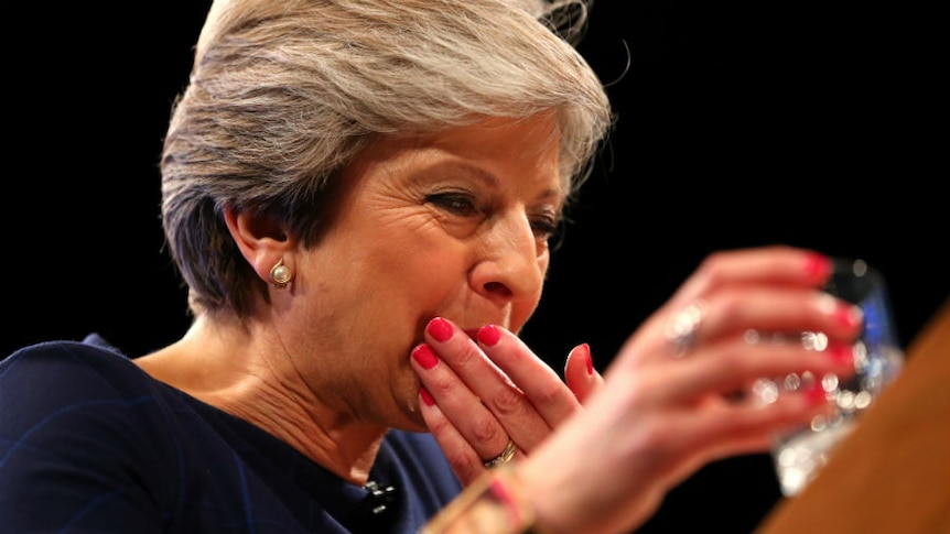 A close-up of Theresa May taking a cough lolly with a glass of water,