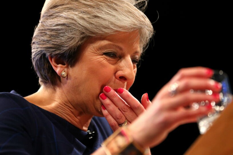 A close-up of Theresa May taking a cough lolly with a glass of water,