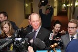 A group of journalists and camera operators surround Fraser Anning in a corridor.