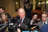A group of journalists and camera operators surround Fraser Anning in a corridor.