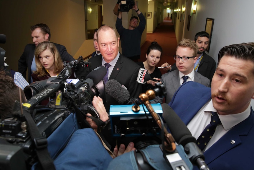 A group of journalists and camera operators surround Fraser Anning in a corridor.