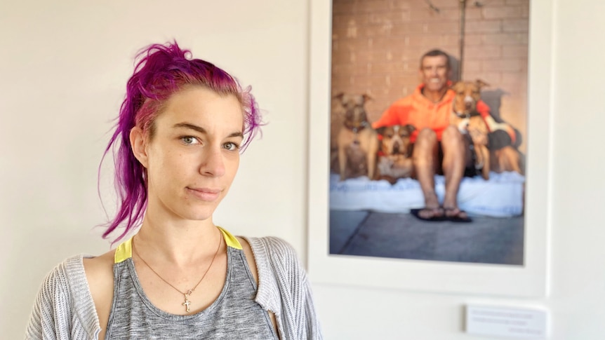 A woman stares into the camera with a photograph on the wall behind her.