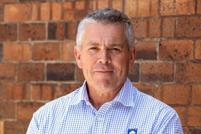 A man in a blue check shirt standing in front of a brick wall.