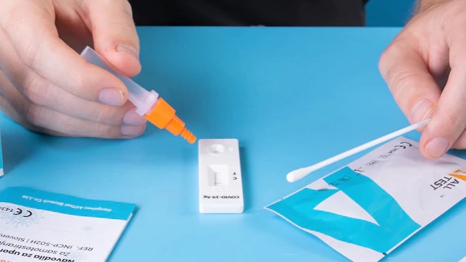 A person holding a Rapid Antigen Test on a blue desk