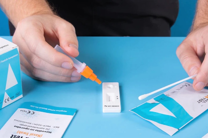 A person holding a Rapid Antigen Test on a blue desk