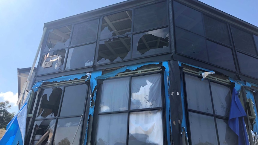 A two story house with lots of glass windows, most smashed by hail.