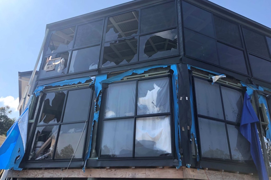 A two story house with lots of glass windows, most smashed by hail.