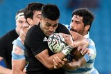 An All Blacks player holds the ball to his chest as he is tackled by two Argentine opponents.