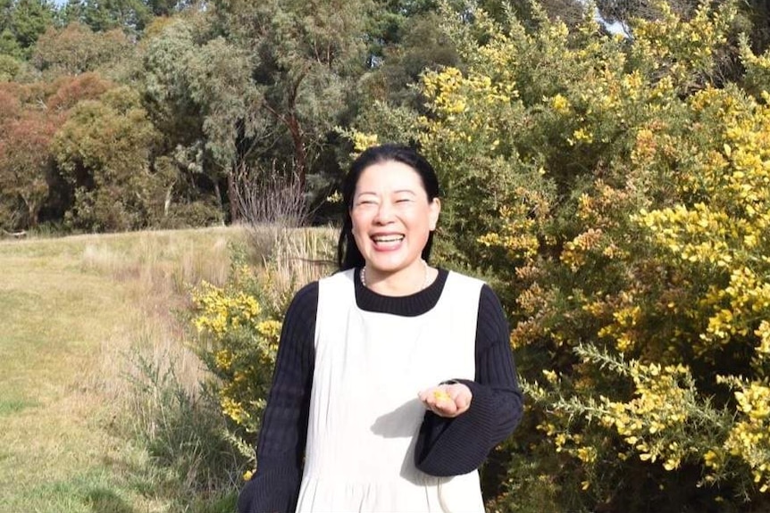Chen Shi standing in the sun surrounded by trees and laughing.