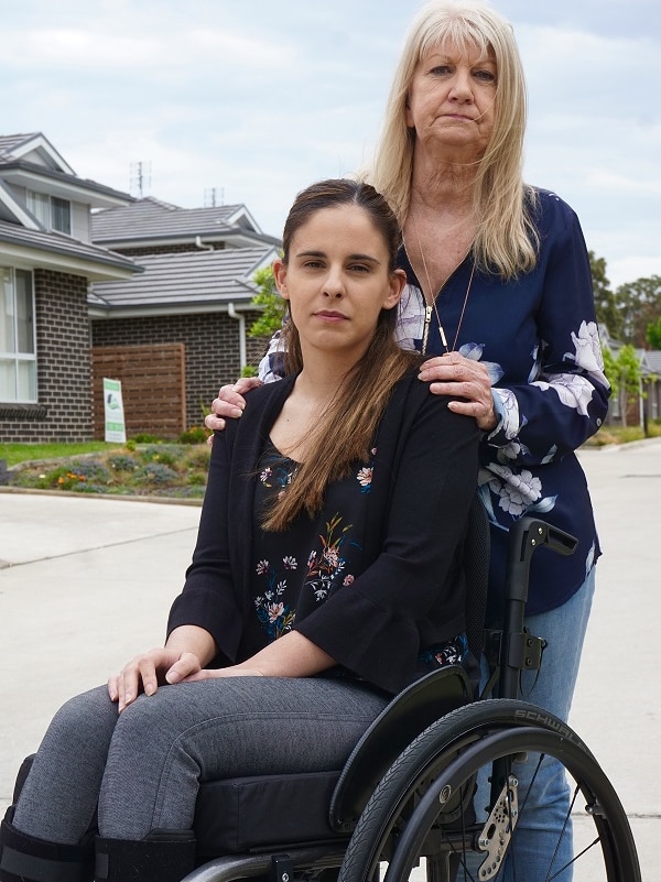 A woman stands behind another woman in a wheelchair