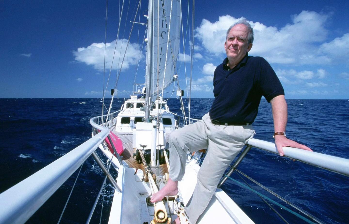 A white man stands on a sailboat while looking out to sea.