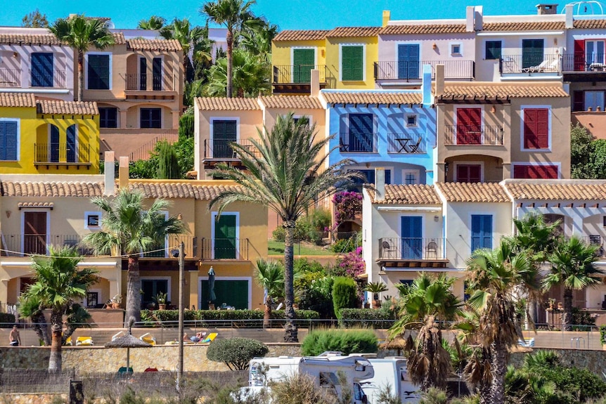 On a bright sunny day, you view multi-coloured terrace homes cascading down a hill to a beach.