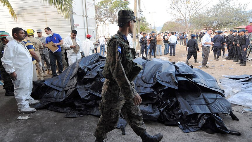 A Honduran soldier stands guard as forensic workers remove corpses