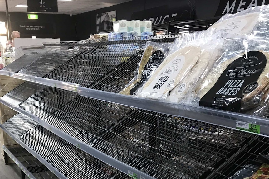 Shelves in a supermarket are bare except for a few packets of pizza bases.