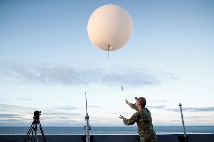 A person in military camo lets go of a weather balloon. 